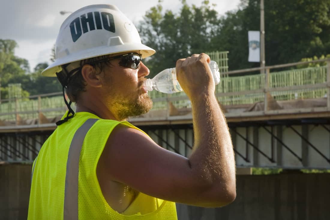 un ouvrier du bâtiment boit dans une bouteille d'eau