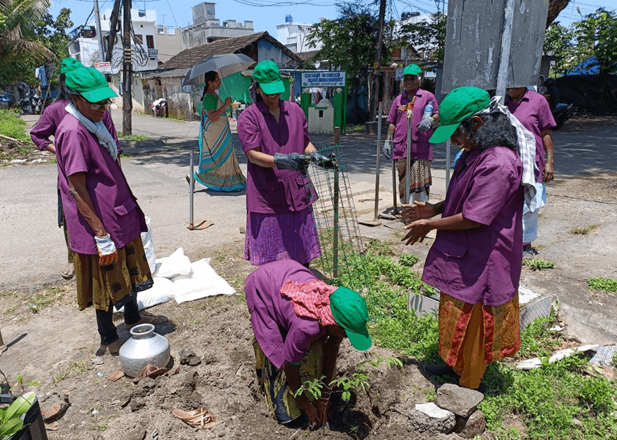 Des femmes portant des chemises violettes et des chapeaux verts plantent des arbres.