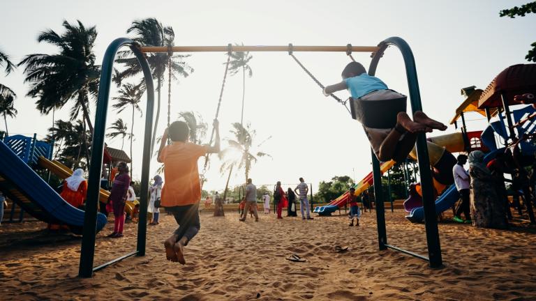 Enfants jouant sur des balançoires dans un parc de quartier bordé d'arbres