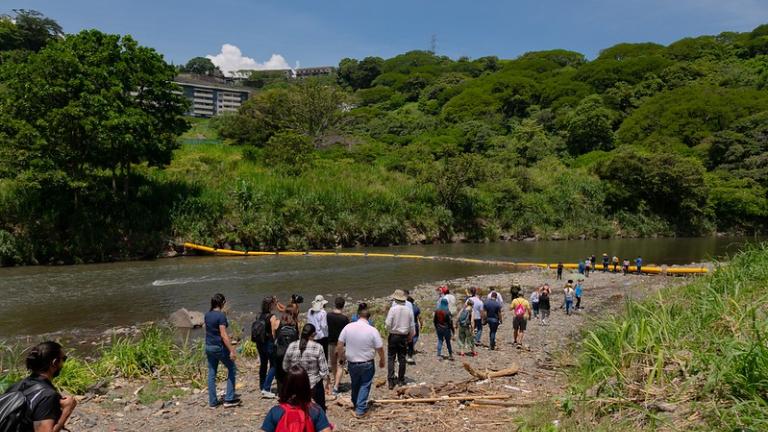 Les participants à la Costa Rica City Academy marchent sur les rives de la rivière Virilla pour voir la barrière de plastique qui retient les déchets.