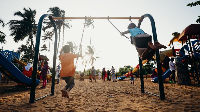 enfants sur une balançoire au coucher du soleil avec des palmiers en arrière-plan