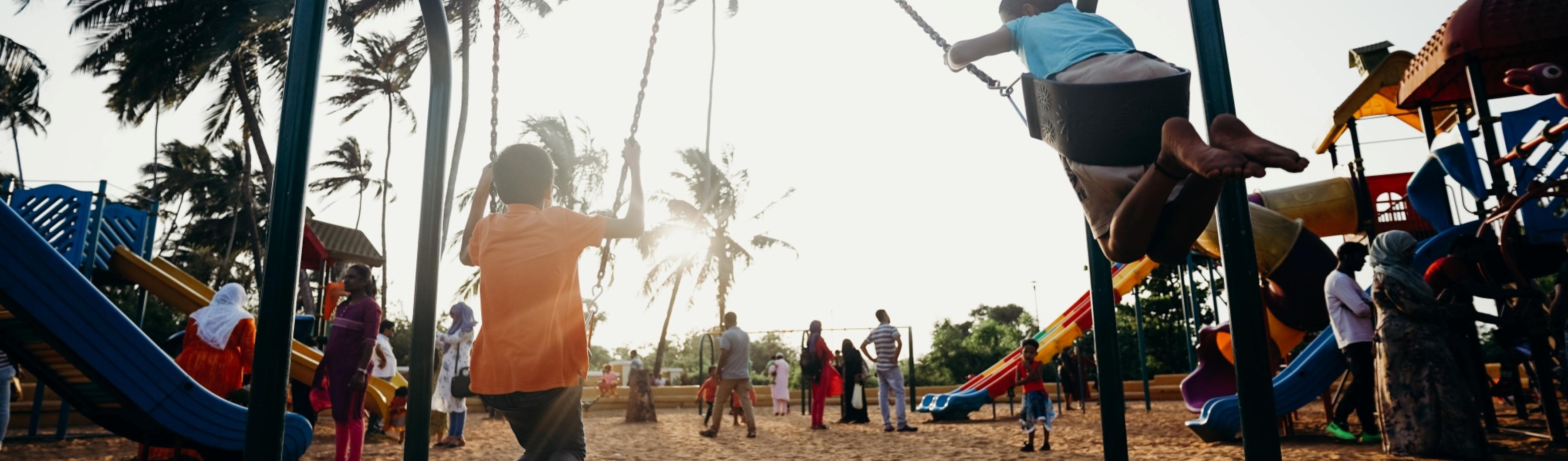 Enfants jouant sur des balançoires dans un parc de quartier bordé d'arbres